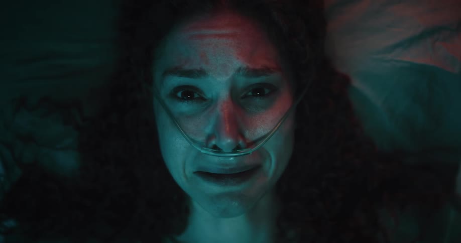 A woman with curly hair wearing a nasal cannula realizes shes in a hospital and starts screaming in disbelief