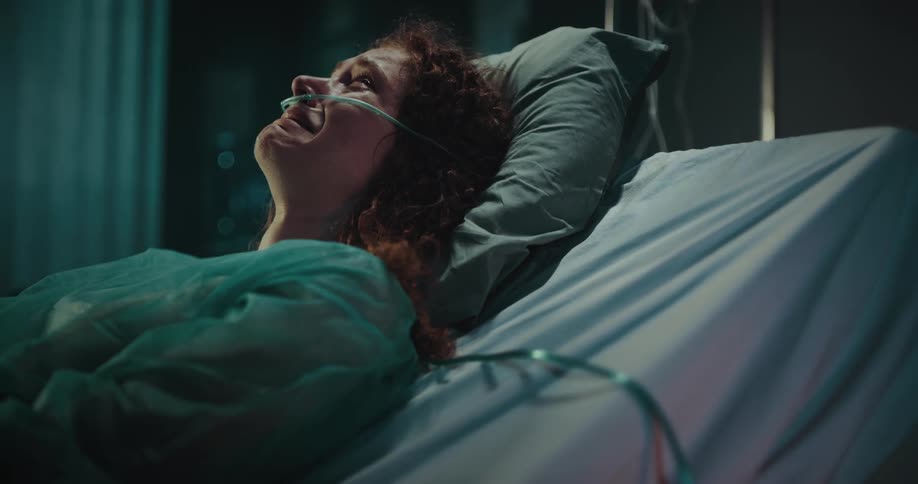 Female patient lying in a hospital bed with a nasal cannula and crying