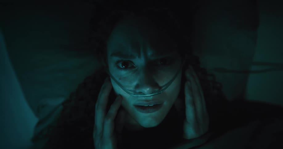 Woman lying on bed feels her nasal oxygen tube with a frown