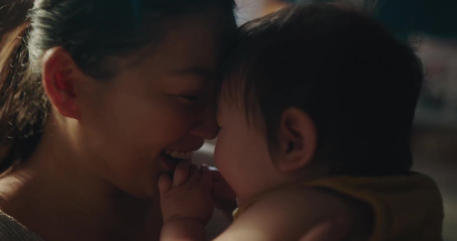 A young mother holds her baby close to her face while laughing and smiling