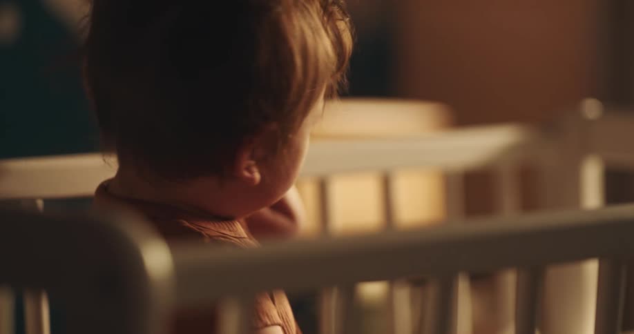 A child girl is playing in a crib and smiles