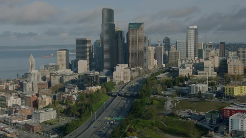 A city with a highway near a body of water on a cloudy day