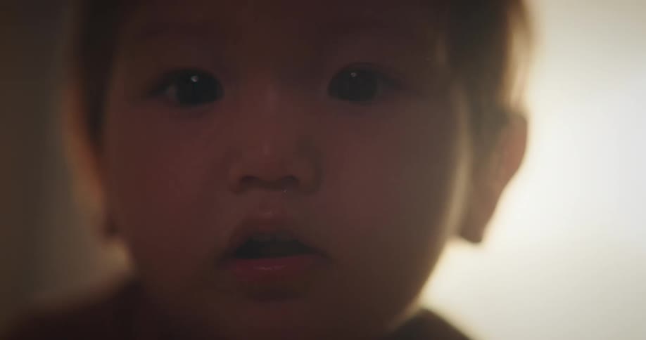 A baby reaching out with one hand and looking back towards a light