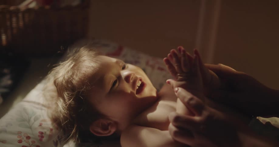 An adult is clapping a baby who is lying down and smiling