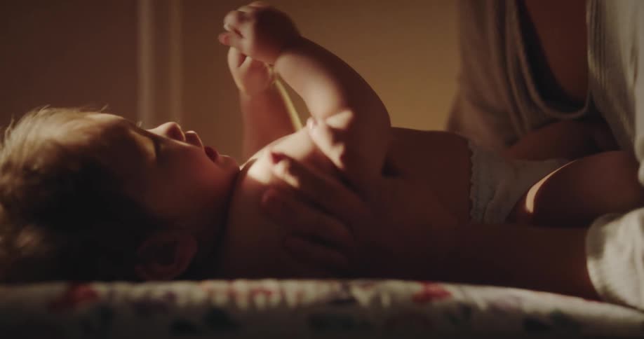A mother caressing her baby who is wearing a diaper and being illuminated by sunlight