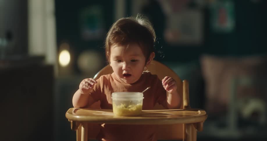 Baby girl sitting in a high chair with a bowl of food in front of her