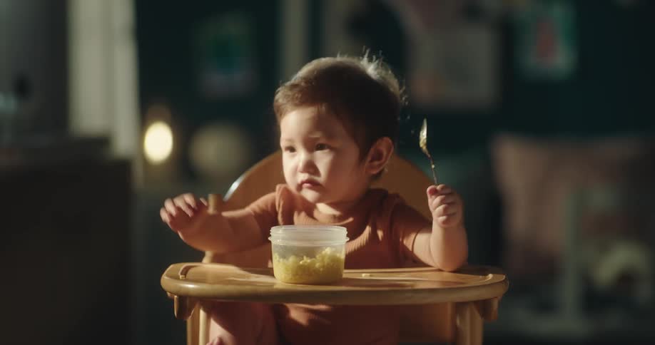 Baby girl sitting eating and holding a spoon with one hand
