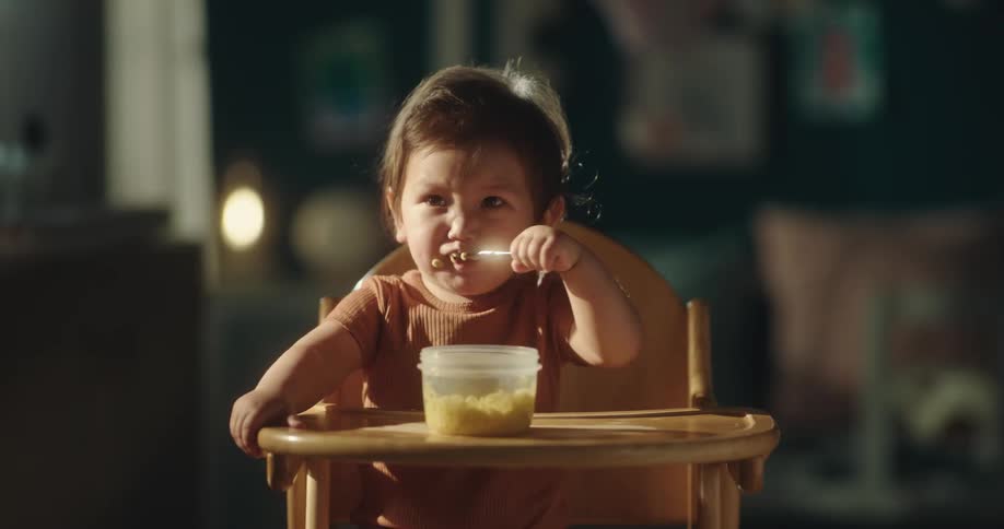 A female child eating food with a small spoon in the morning