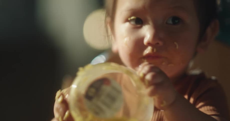 Asian baby girl eating with her hands and holding a bowl