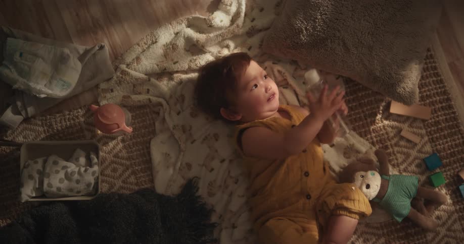 A baby is on her back and turns around and there are several toys around her