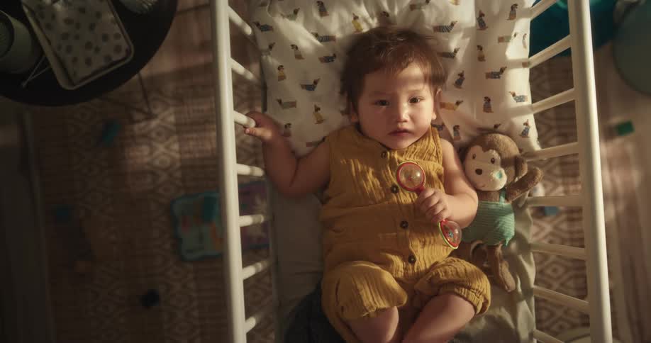 A little baby with a toy in his hand is lying in his crib