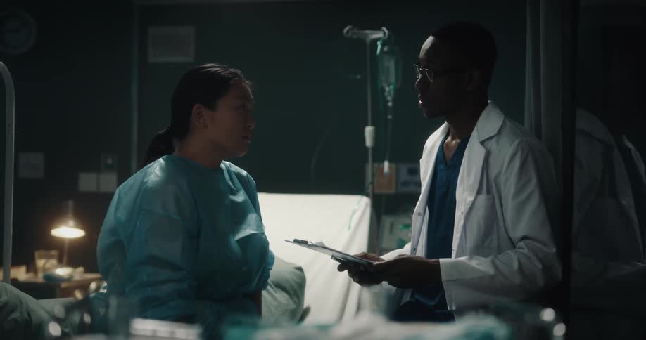 A doctor and a nurse talking in a hospital and behind a hospital bed