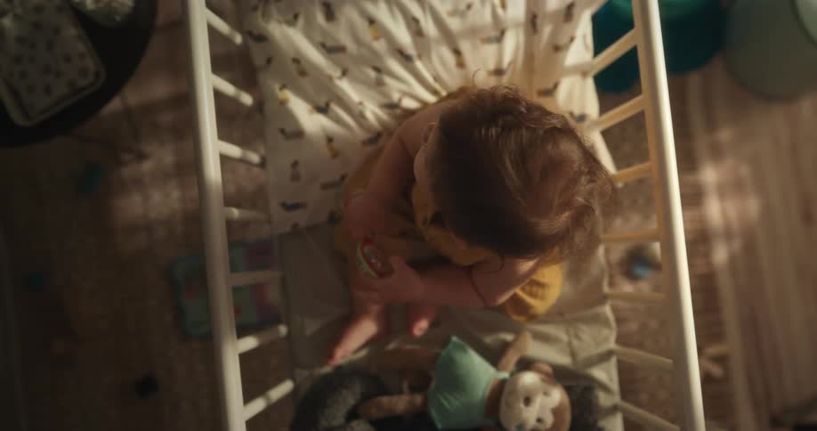 A baby sitting in his crib with a toy in his hand