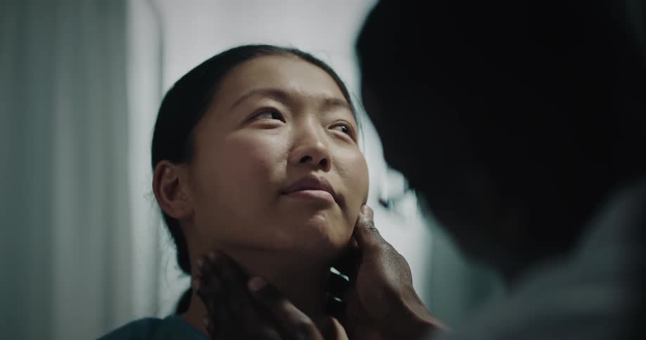 Hands of a black doctor on the neck of as asian patient at midday