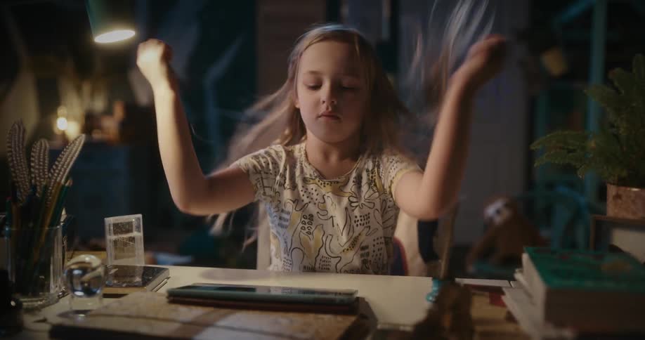 A little girl is sitting at a desk playing with a tablet computer