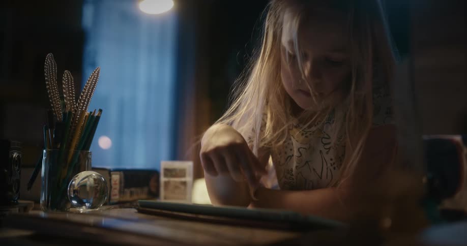 A girl with long blond hair taps on her tablet as she reads at home