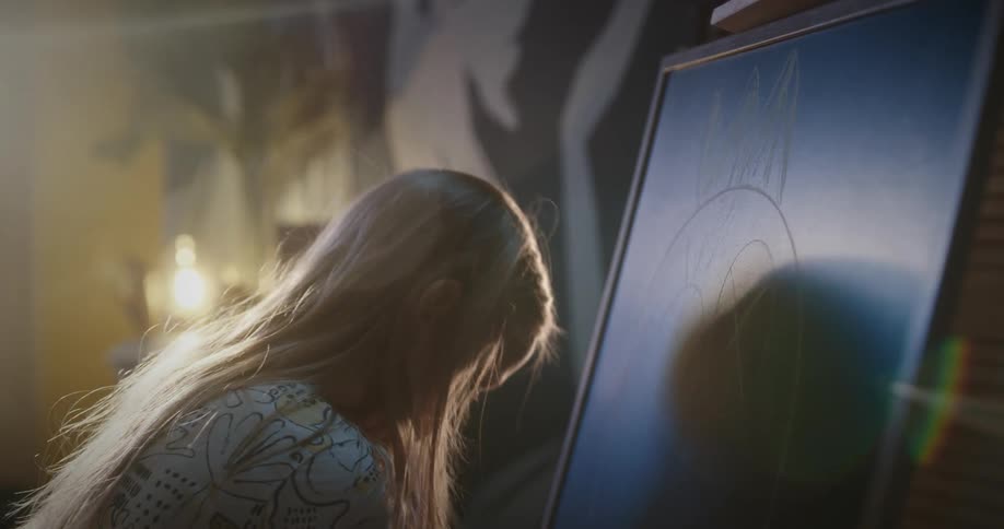 Blonde girl draws on blackboard with colored chalks