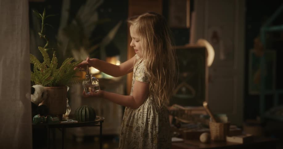 Girl waters an indoors plant using a water spray bottle