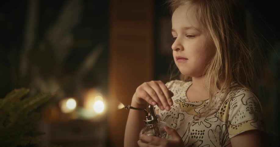 A little blonde girl is spraying water on a plant that is in a vase
