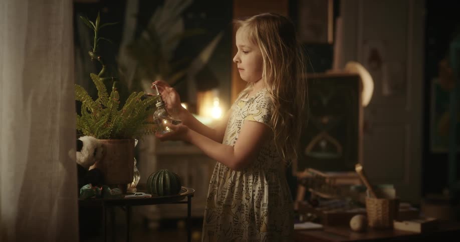 A little blonde girl takes a spray bottle and sprays it on a plant in a pot