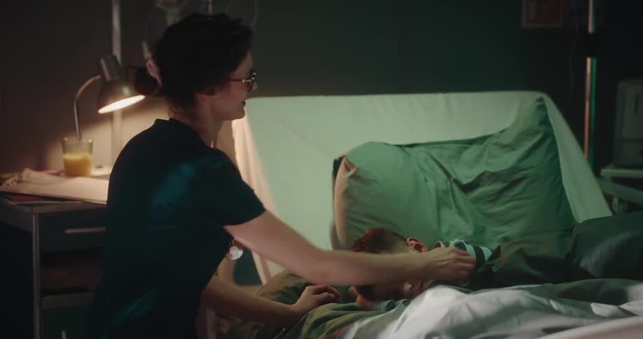 A nurse sitting by a hospital bed being playful with the boy on it