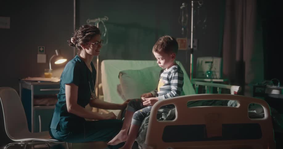 A doctor is petting a little boy who is in a hospital bed