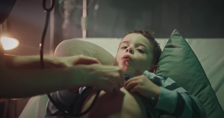 A little boy lifts his pajama top and takes deep breaths as a doctor listens to his chest with a stethoscope