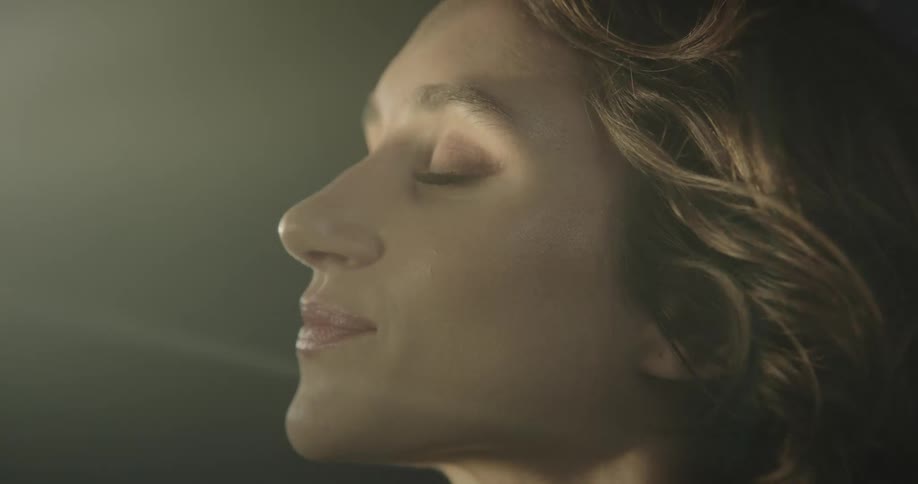 A woman with wavy hair opens her eyes as the sun shines on her face