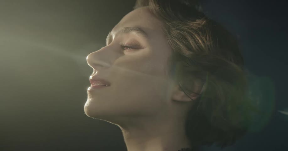 A woman with facial expressions of relaxation as her face is illuminated by a light