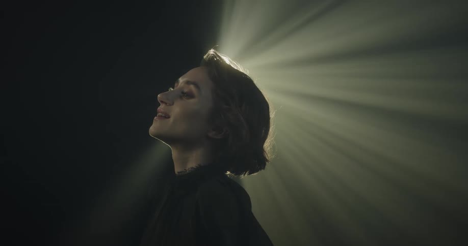 A woman tilts her head and smiles as rays from a glowing light in the distance illuminate the darkness during a near death experience