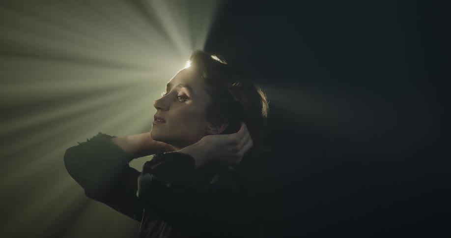 A woman runs her fingers through her hair while a projector light shines on her