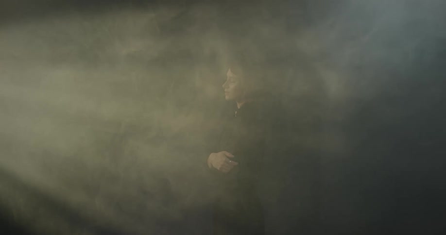 Woman stands in a room filled with smoke under moving lights