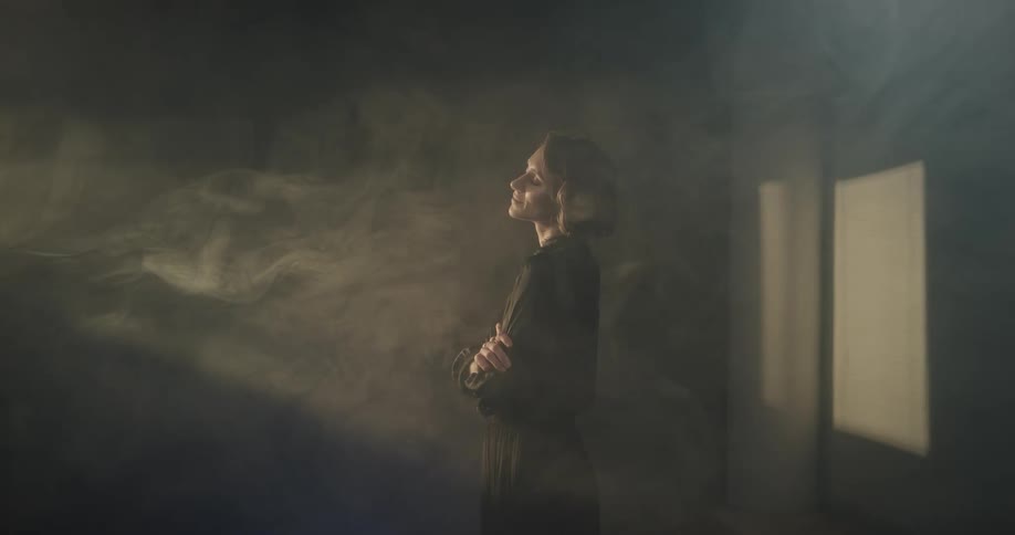 Woman stands in a room filled with smoke under moving lights