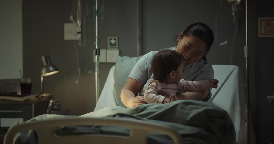 An asian woman playing with her kid while sitting on an hospital bed