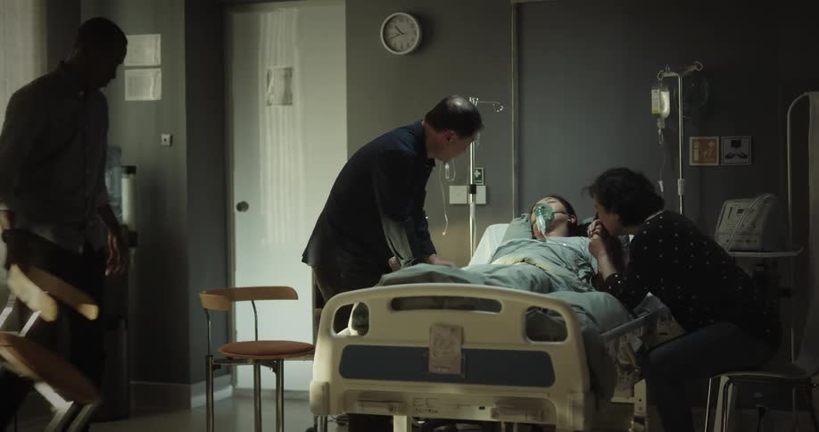 People sitting beside a woman who is bedridden in a hospital room