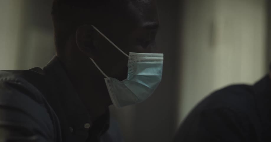 A black man and an asian man are wearing masks sitting next to each other