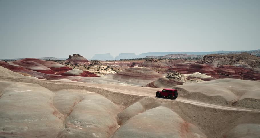 Aerial view of a red suv driving through desert geological areas