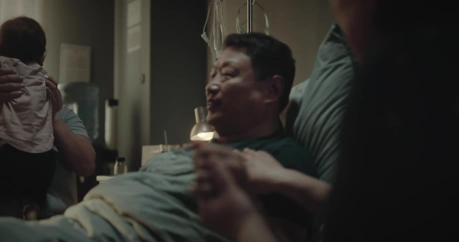 Patient lying in the hospital room with their family beside them and a baby on top of them
