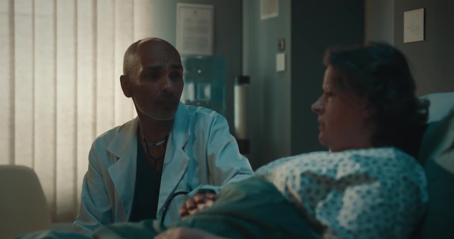 Doctor sitting beside a woman lying on a bed looking concerned