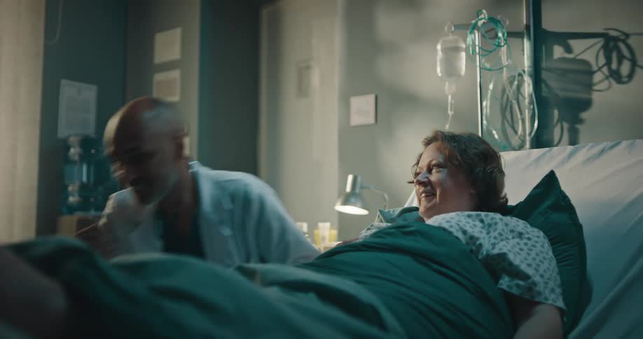 Doctor talking to a patient who is signing a medical record while lying in a hospital bed