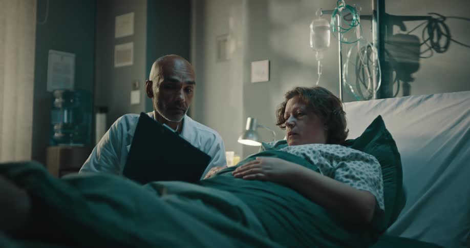 A doctor explains a medical chart to a woman laying in a hospital bed