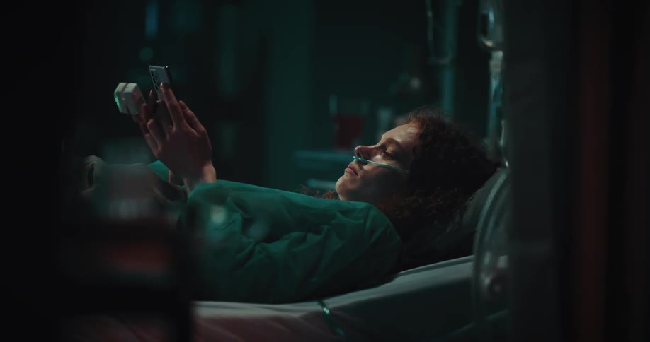 Female patient lying in a hospital bed making a phone call