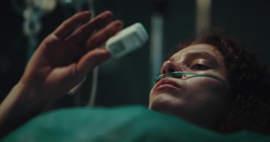 Female patient lying in hospital bed examines finger air monitor she is wearing