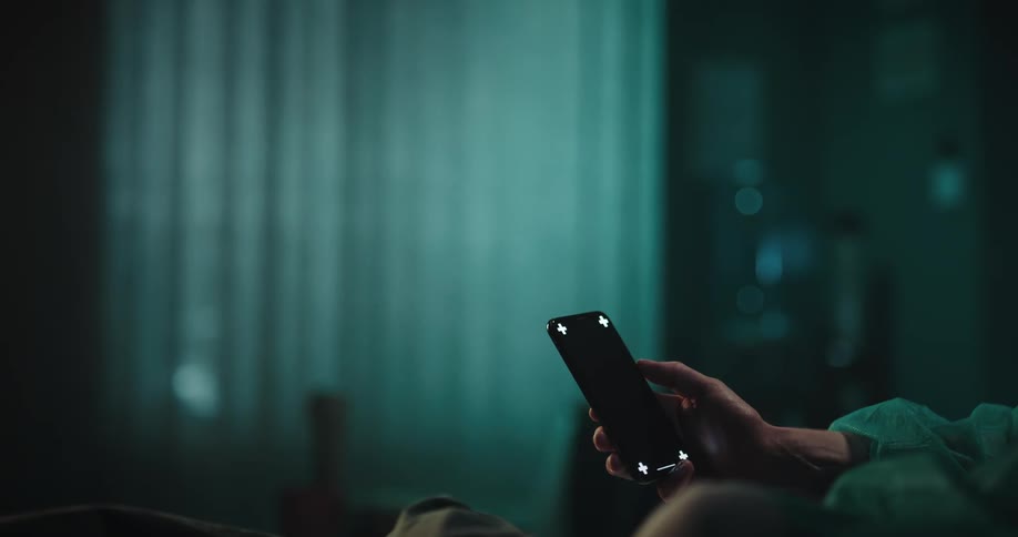 A man is holding a cell phone and moving his thumb across the black screen
