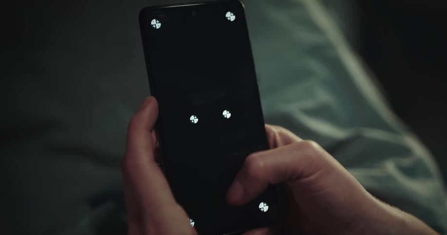 A woman holds a cellphone with both hands and moves her thumb across the black screen