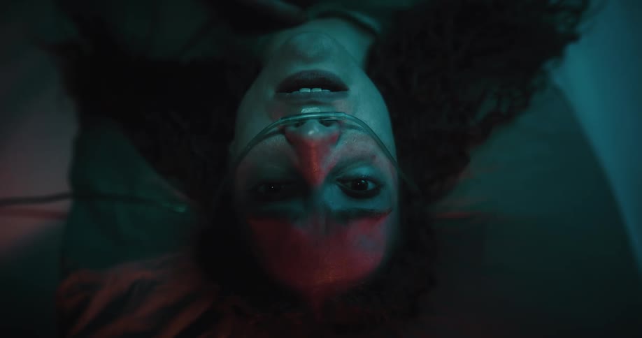 A woman lying down has a medical device on her nose and touches her cheeks with her hands