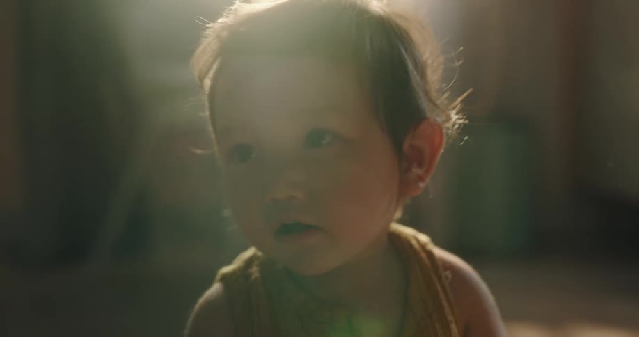 A toddler sits on the floor with a book in her hand smiling