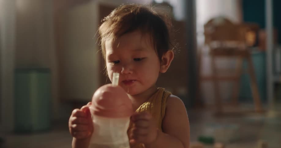 Baby girl sitting on the floor playing with toys and drinking water from a bottle