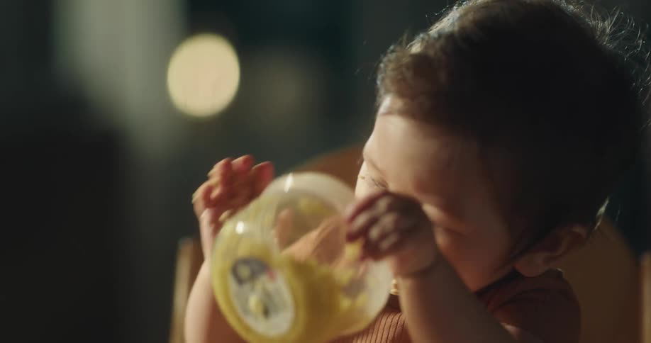 Asian baby sitting in a chair and at a table eating with hands from a small bowl
