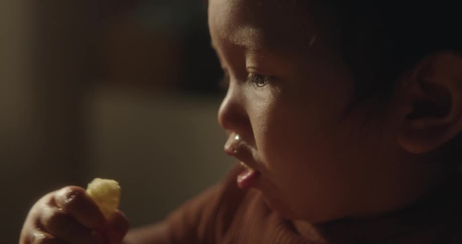 A toddler eating something from his hand